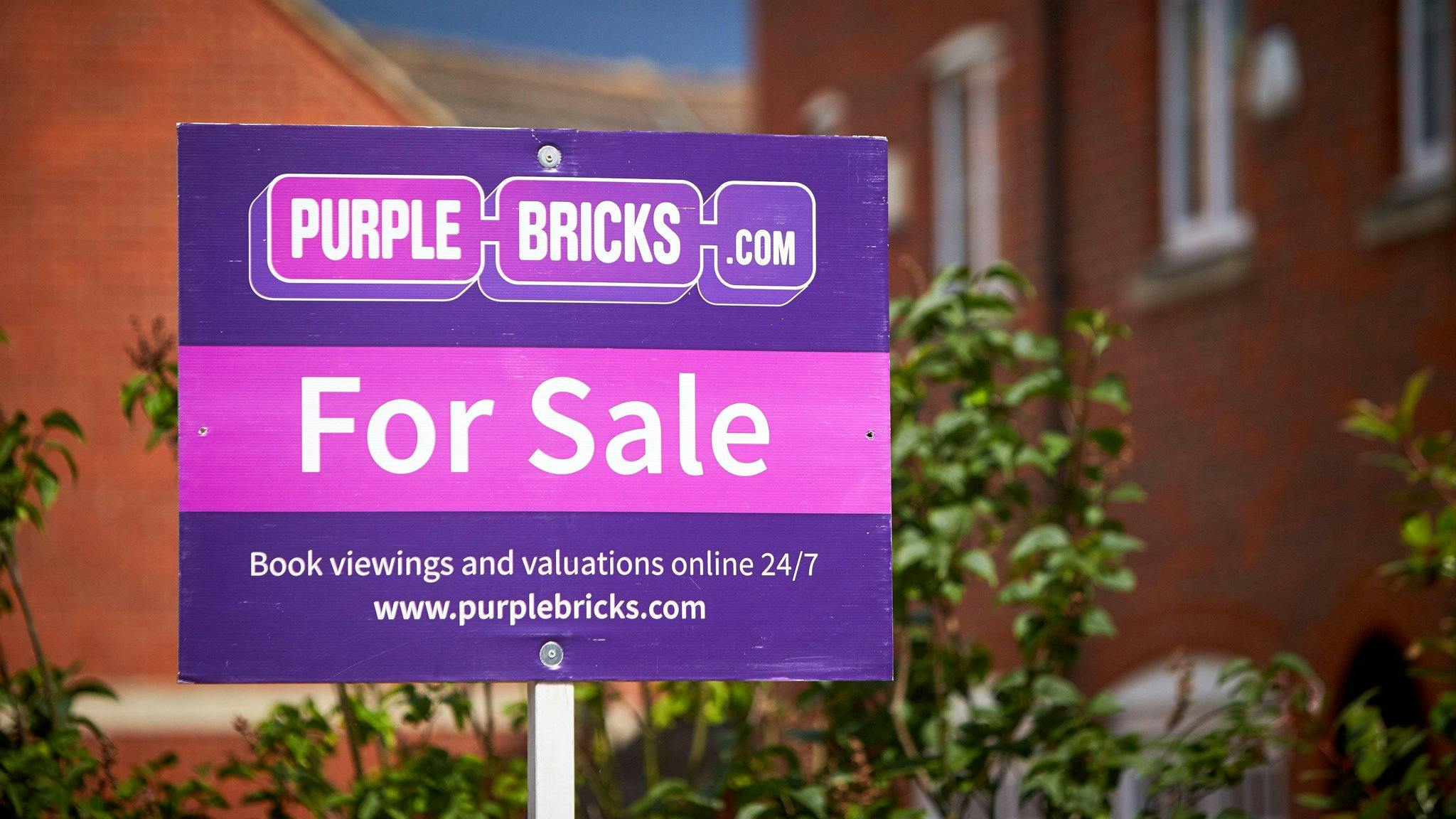 a purple bricks for sale sign outside an unsold house 